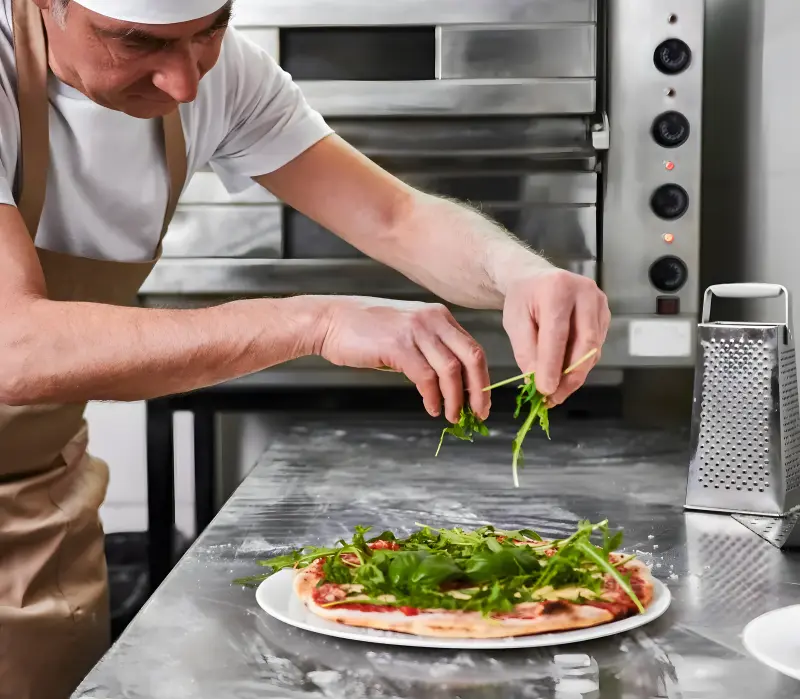 A chef scattering fresh rocket over a pizza