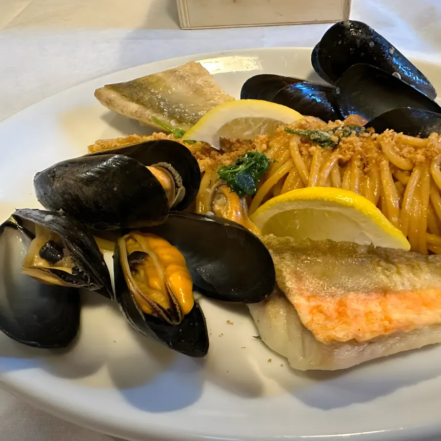 Spaghetti with mussels, grilled fish fillet and a lemon wedge.
