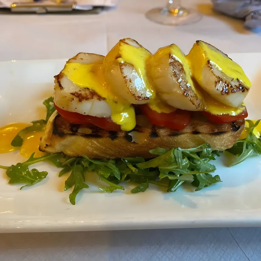 Three seared scallops on grilled bread with a yellow sauce, on rocket.