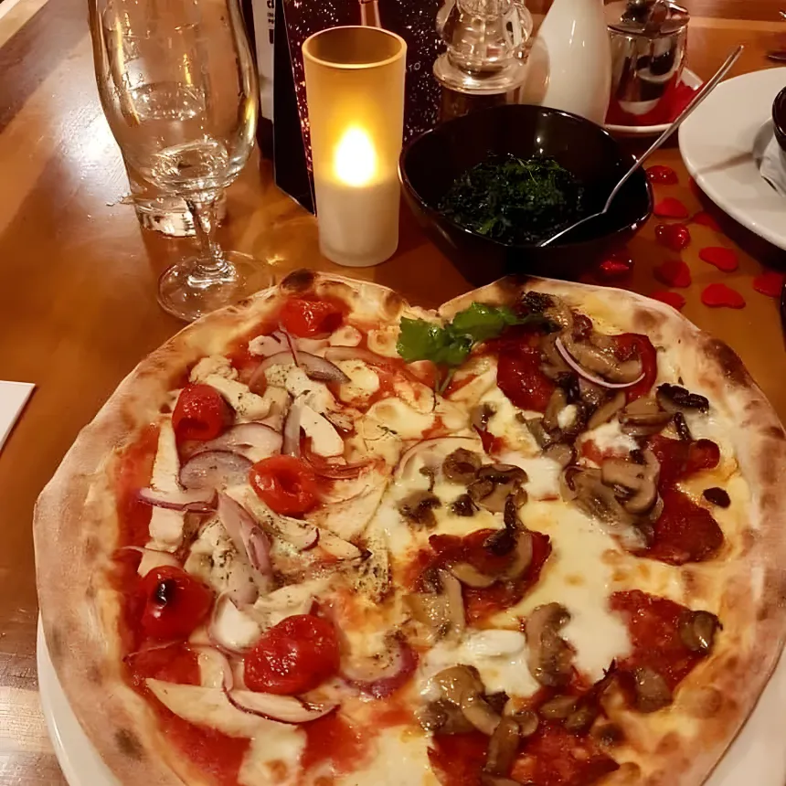 A heart-shaped pizza with melted mozzarella, pepperoni and mushroom on one half and chicken, cherry tomato and red onion on the other.
