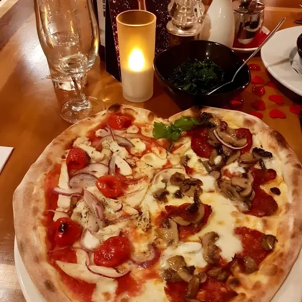A heart-shaped pizza, one half pepperoni and mushroom, the other chicken, cherry tomato and red onion.