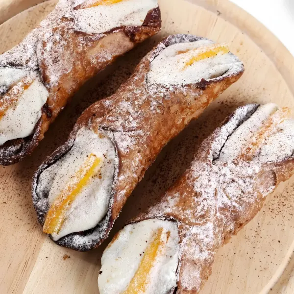 Three ricotta cannoli with powdered sugar and candied orange peel.
