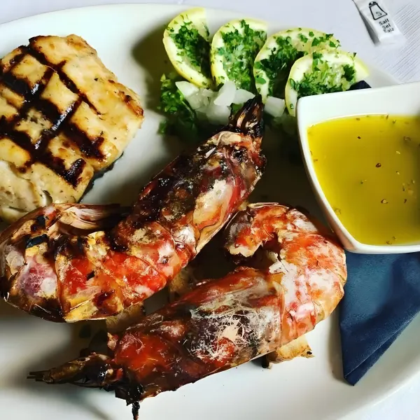 Grilled fish fillet and two large grilled prawns with grilled lemon halves and a pot of lemon butter sauce.