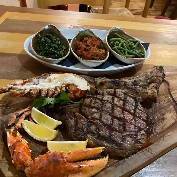 Grilled steak with half a lobster tail and three small bowls of vegetables.