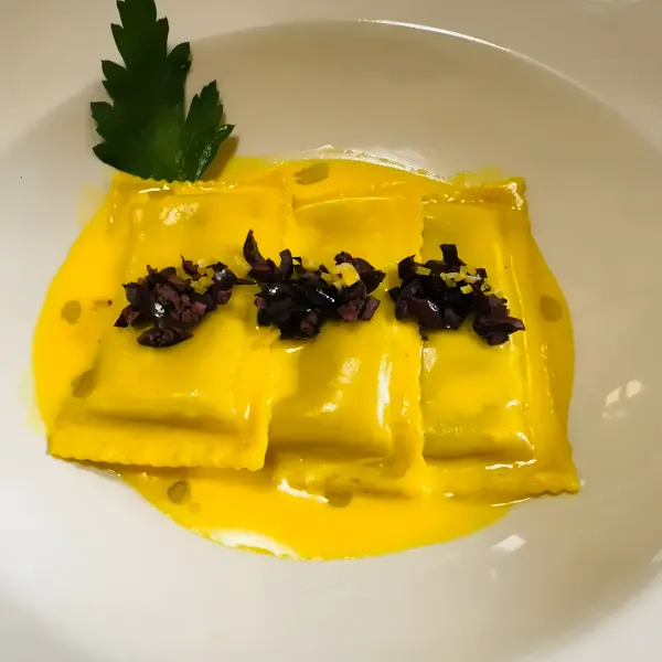 Ravioli in a bright yellow sauce topped with chopped olives.