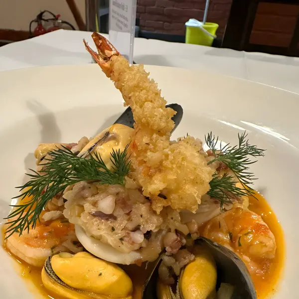 Seafood risotto topped with mussels, prawns and a tempura prawn, garnished with dill.